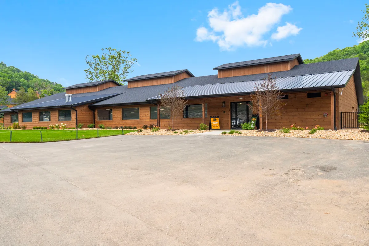 A modern wooden cabin with a landscaped front yard, expansive windows, and a sturdy metal roof. The porch is perfect for gatherings, and the setting suggests a welcoming and serene environment ideal for group get-togethers.