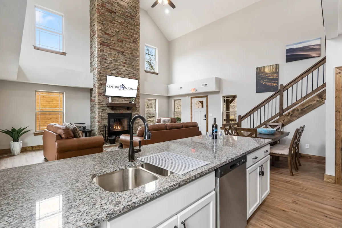 A cozy interior highlighted by a rustic stone fireplace, granite countertops, and a staircase, creating a welcoming atmosphere for family bonding. The fireplace becomes a natural gathering point, echoing the description of cozy movie nights and celebrations around the fire. Modern amenities and homey touches are balanced, enhancing comfort and functionality.