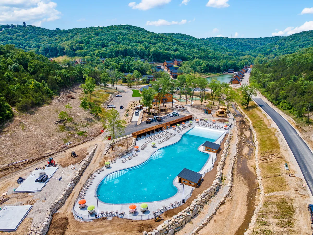 A sparkling swimming pool surrounded by lush greenery, with modern cabins and patio seating nearby. The area encourages swimming, sunbathing, and socializing in a relaxed, resort-like setting.