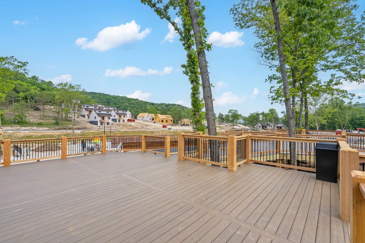 A tranquil wooden deck surrounded by lush trees, with comfortable outdoor seating arranged for gatherings and relaxation. The deck looks out onto scenic rolling hills and neighboring homes, capturing the essence of al fresco living in harmony with nature.