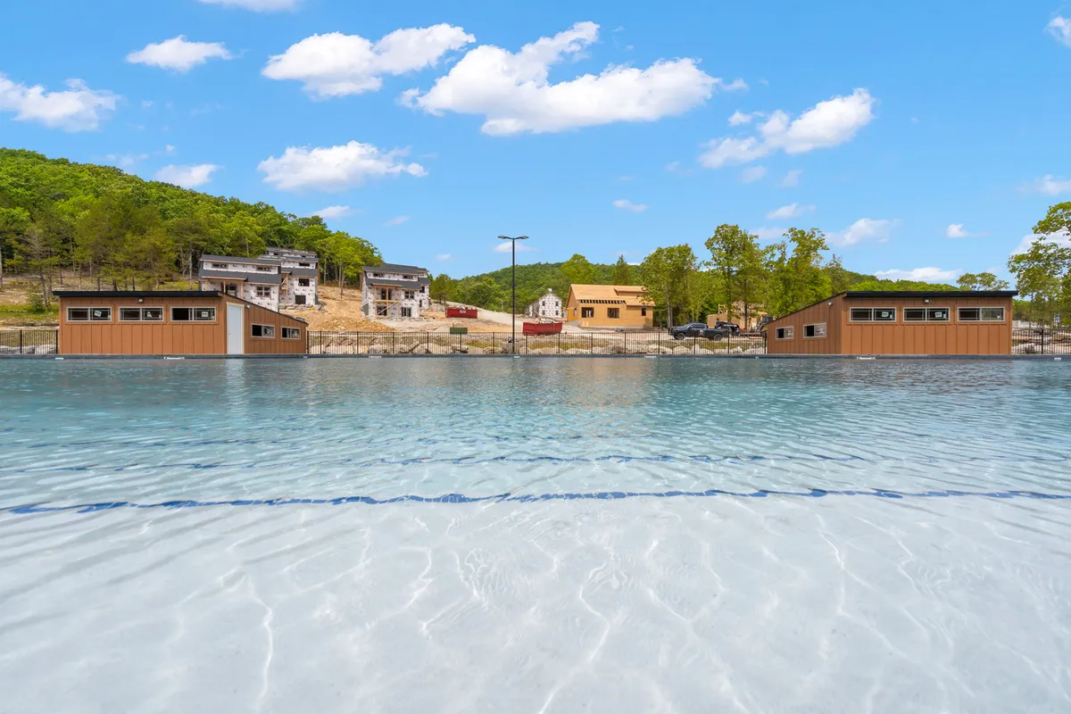 A serene lakefront scene with clear water bordered by wooded hills and lakefront structures. The area looks perfect for boating, fishing, and quiet reflection, with the morning light illuminating the water and nearby forest.