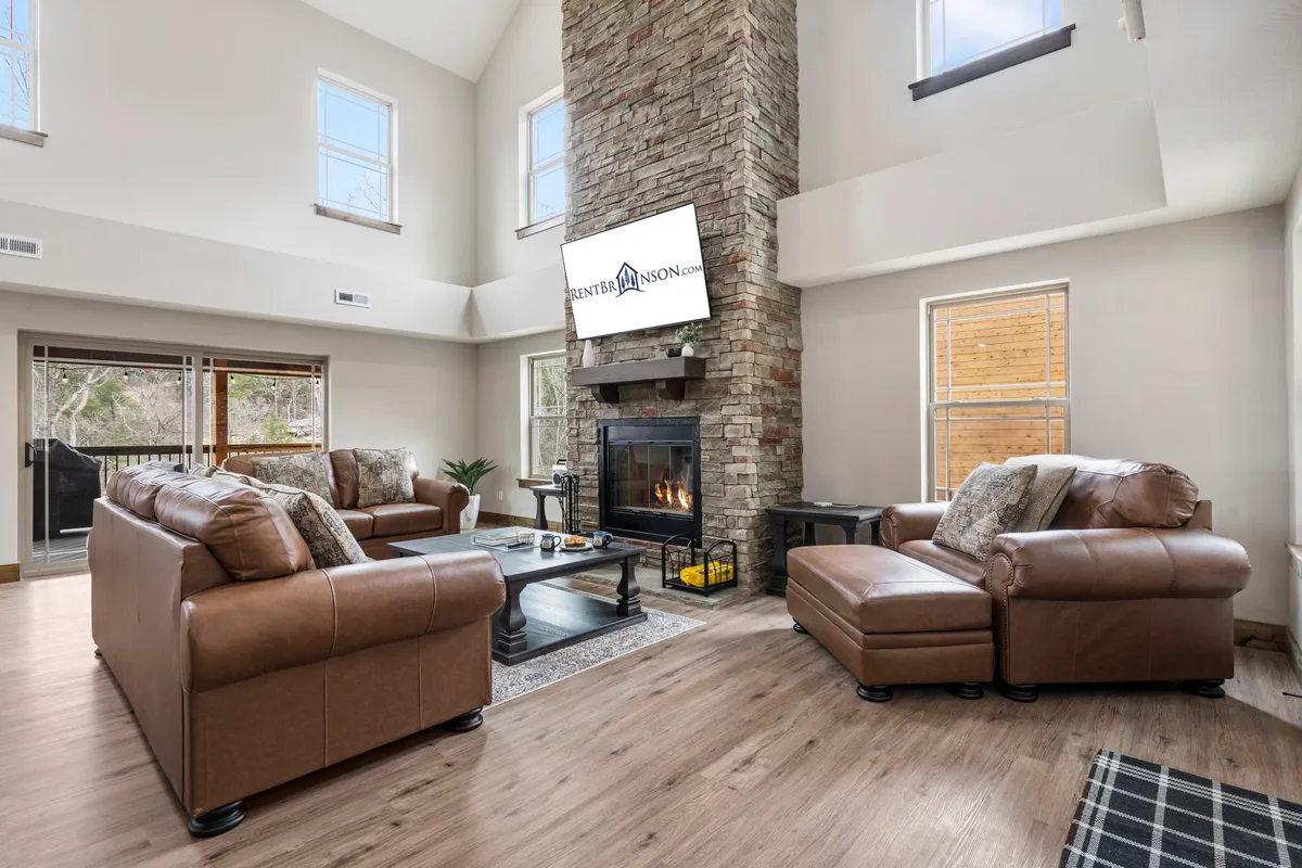 The image showcases a warm, inviting living room with a striking stone fireplace as the centerpiece. Plush leather sofas are arranged for gathering, complemented by a modern television and a rustic coffee table, setting the scene for relaxation, movie nights, and family bonding.