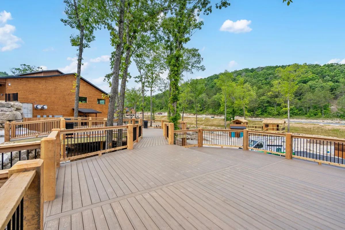 A spacious wooden deck surrounded by tall trees and rolling hills in the distance. The deck is positioned for scenic viewing, relaxation, and socializing, with the tranquil forest backdrop inviting guests to connect with nature or gather for evening stories.