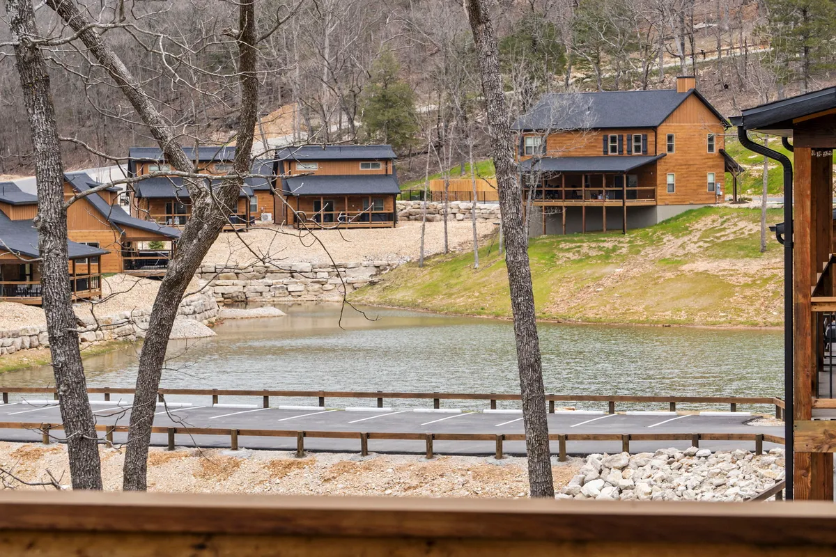 A tranquil lake scene with cabins nestled among trees, capturing a quiet moment perfect for fishing, picnicking, or hiking along the shore. The relaxed mood and scenic beauty emphasize the natural amenities available.