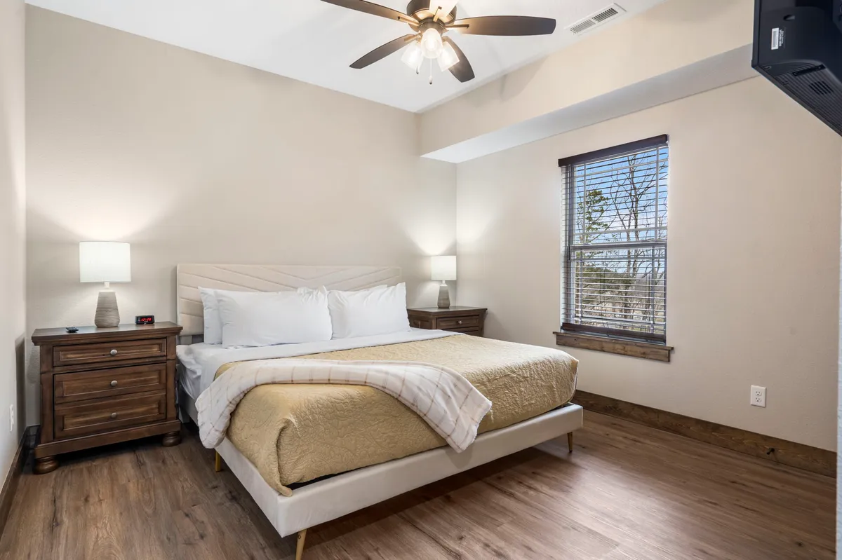 A serene bedroom with a plush bed, flanked by nightstands and soft lighting from lamps. Large windows let in natural light, creating a tranquil space for restful sleep or leisurely mornings in bed.